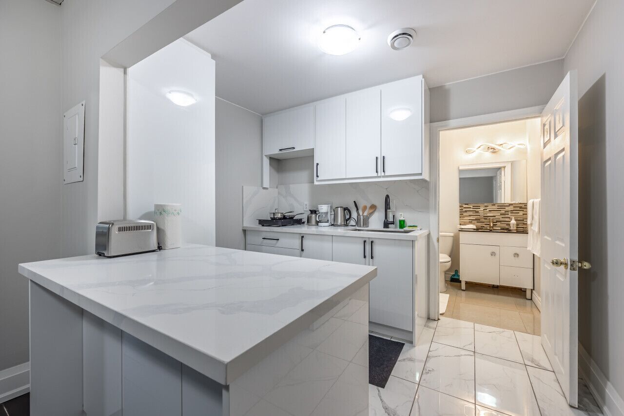 Een moderne keuken met witte kastjes, een centraal eiland en uitzicht op de aangrenzende badkamer.