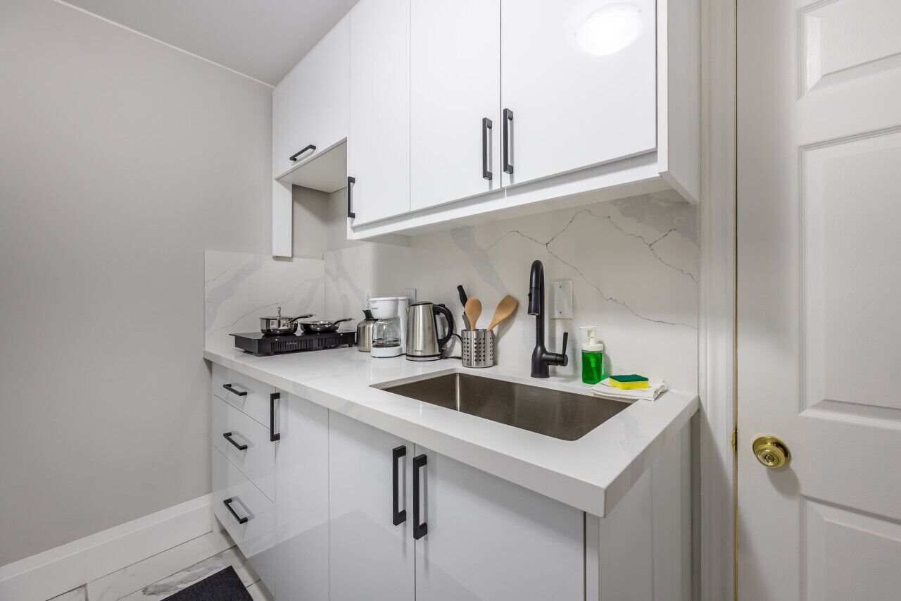 A modern kitchen with white cabinets, a stainless steel sink, and various kitchen appliances.