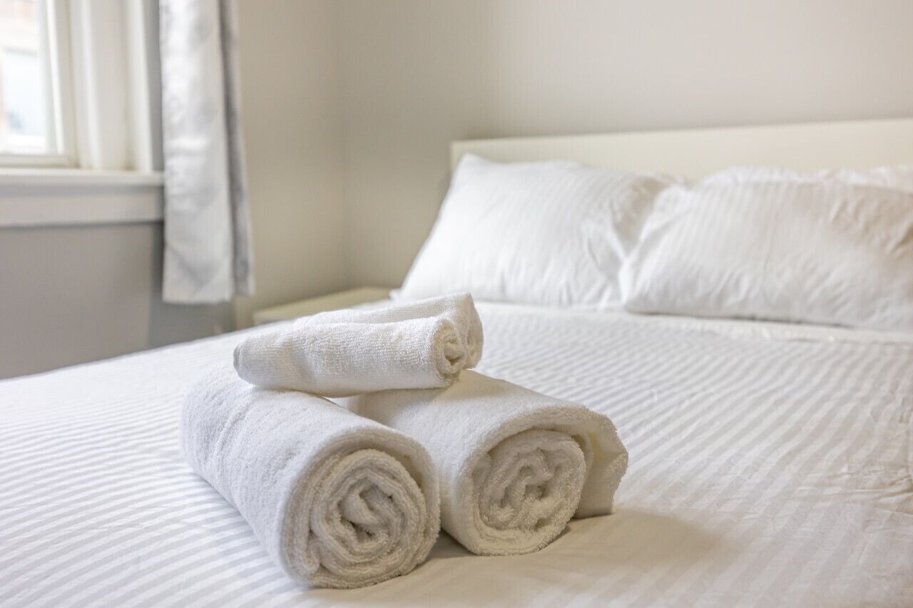 Un lit bien fait, avec des serviettes blanches pliées en rouleaux et une tête de lit blanche.