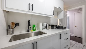A modern kitchen with white cabinets, a stainless steel sink, and various appliances including a coffee maker and toaster. - Serenity by the Falls: Modern 2 Bedroom Hideaway (Niagara Falls)