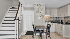 A modern kitchen with a wooden staircase, a dining area with a table and chairs, and a kitchen island. - Stylish Mississauga Lower Unit BBQ Yard Paradise (Mississauga)