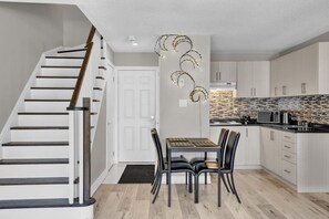 Eine moderne Küche mit einer Holztreppe, einem Essbereich mit Tisch und Stühlen sowie einer Kücheninsel.