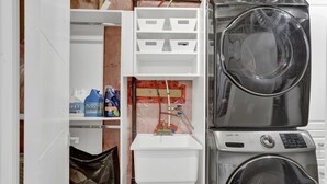 A laundry room with stacked washers and dryers, a water heater, and storage shelves with cleaning supplies. - Stylish Mississauga Lower Unit BBQ Yard Paradise (Mississauga)