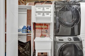 Ein Waschraum mit gestapelten Waschmaschinen und Trocknern, einem Warmwasserbereiter und Regalen mit Reinigungsmitteln.