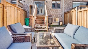 A patio area with wicker furniture and a glass table, surrounded by a brick building with wooden fences. - Stylish Mississauga Lower Unit BBQ Yard Paradise (Mississauga)