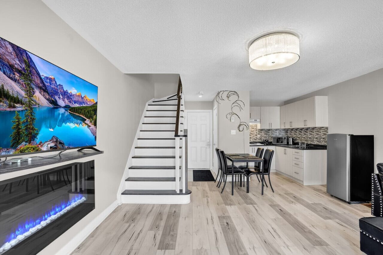 A modern kitchen with white cabinets, a stainless steel refrigerator, and a dining area with a black table and chairs.