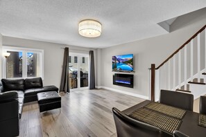 Ein modernes Wohnzimmer mit einer Eckcouch, einem Esstisch mit Stühlen, einem flachbildfernseher an der Wand und einer Treppe mit Holzbalkonen.