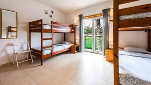 Quarto com beliches, uma escrivaninha, uma cadeira e janela com vista para o verde.