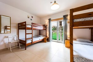 Ein Zimmer mit Etagenbetten, einem Schreibtisch, einem Stuhl und einem Fenster mit Blick auf Grünflächen.