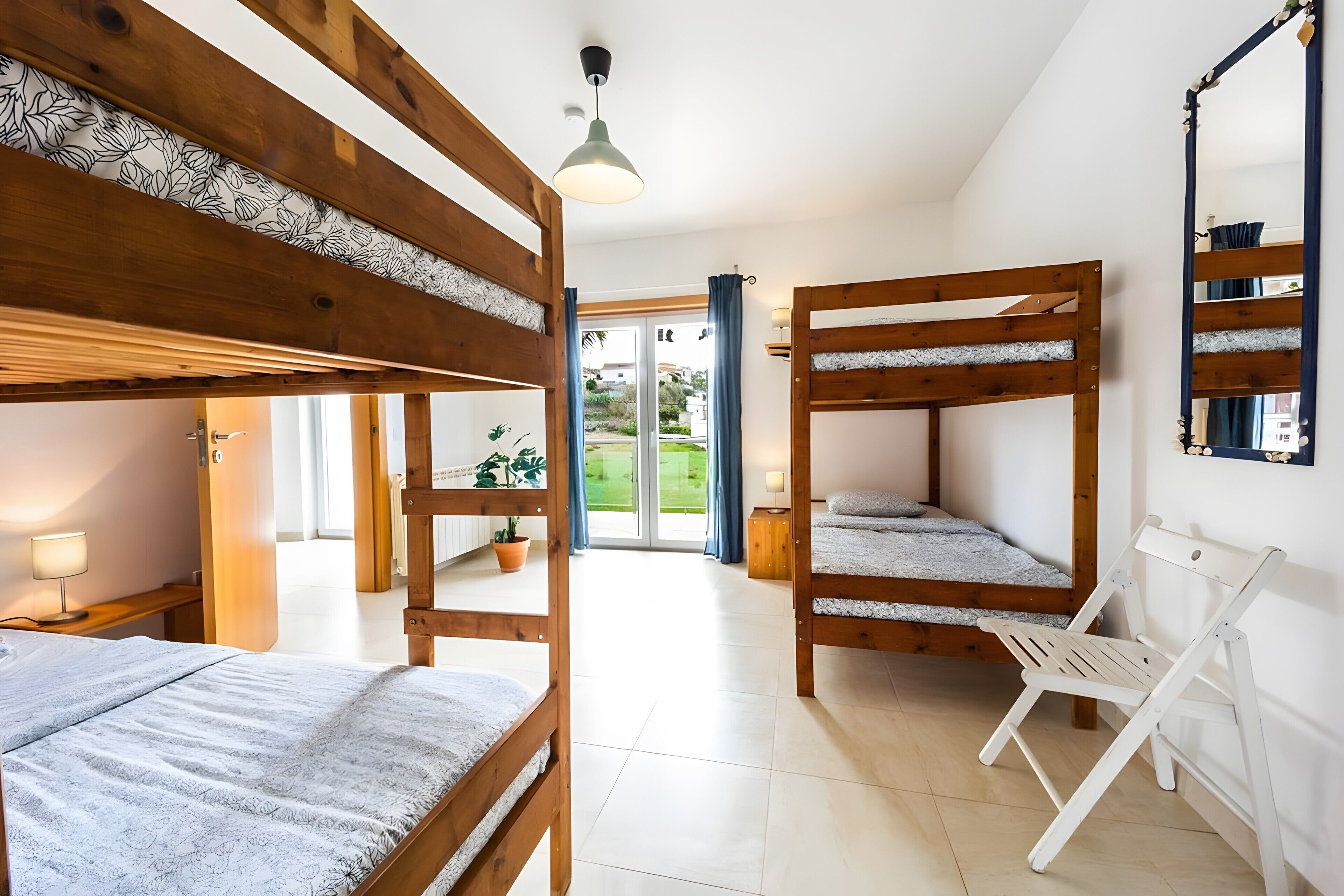 A bunk bed room with a wooden ceiling, a small table with a lamp, and a view of the outdoors through a glass door.