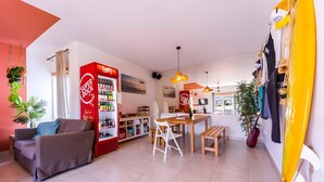 Um espaço de estar moderno com um sofá, uma mesa de jantar com cadeiras, uma cozinha e uma prancha de surf.