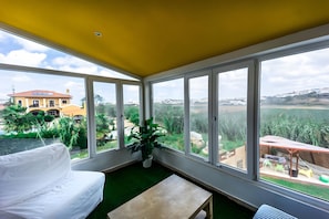 Ein Zimmer mit einem weißen Sofa, einem kleinen Tisch und großen Fenstern mit Blick auf ein gelbes Gebäude und Grünflächen.