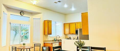 A compact kitchen with wooden cabinets, a dining area with a table and chairs, and a ceiling fan.