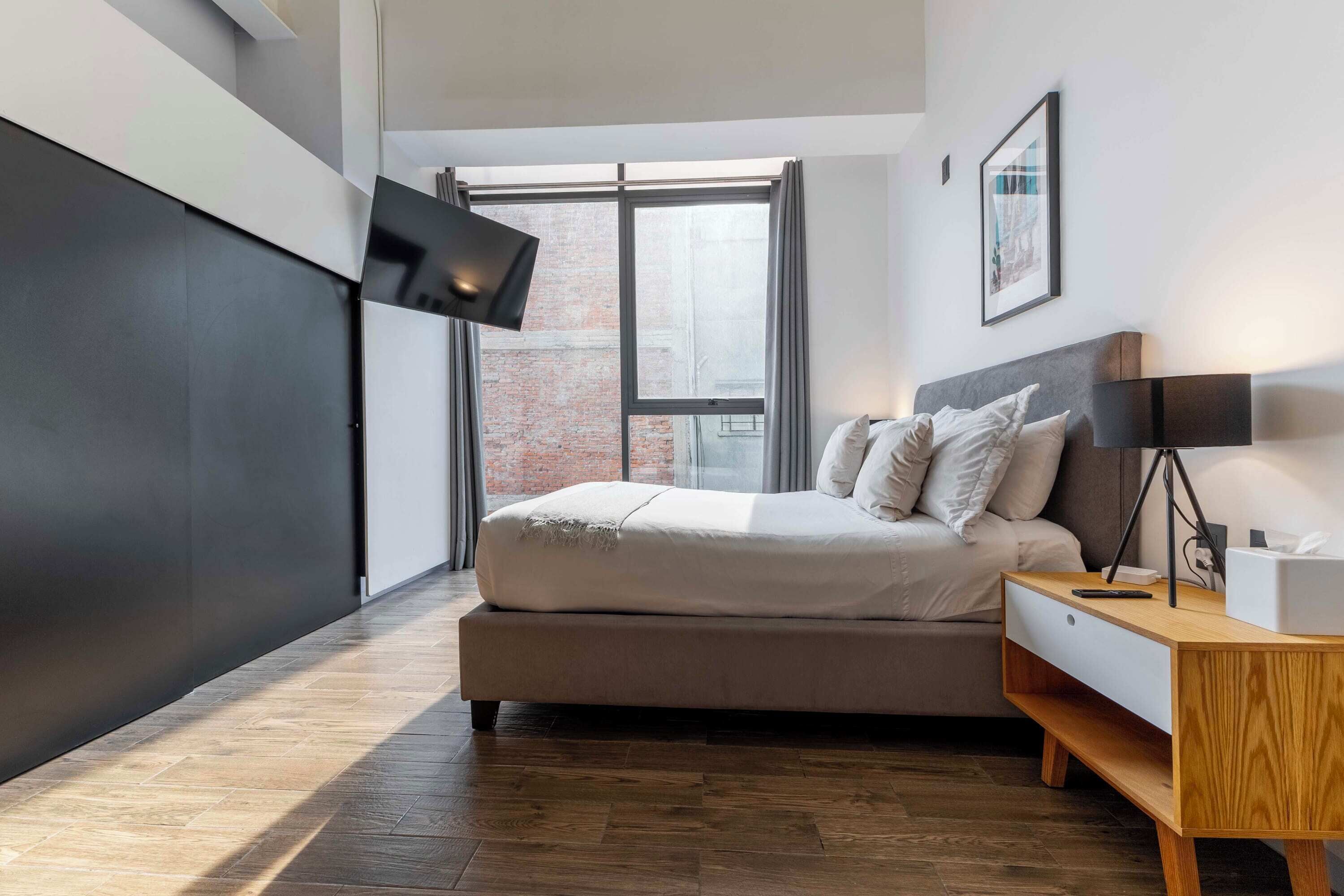 A modern bedroom with a bed, bedside table, and a TV mounted on the wall.