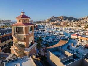Een hotel aan de kust met een opvallende toren, een jachthaven met tal van boten, en een achtergrond van heuvels.