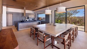 A modern kitchen with a central island, wooden chairs, and pendant lighting. - Diamante Beach Estate 47 (Cabo San Lucas)