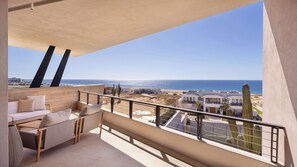A balcony with a sofa and chairs, overlooking a beach and buildings. - Diamante Beach Estate 47 (Cabo San Lucas)