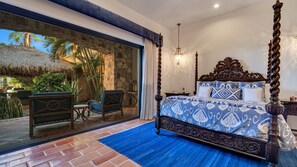 Ein Schlafzimmer mit einem Himmelbett, einer Steinwand und Blick auf einen tropischen Garten.