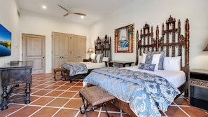 A bedroom with a large bed, a smaller bed, a desk, and a chair. There is a painting on the wall and a ceiling fan. - Hacienda Beach Club 1100 (Cabo San Lucas)