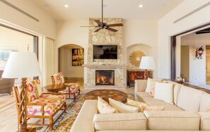 A spacious living room with a fireplace, a ceiling fan, and a television mounted on a stone wall. - Diamante Golf Villa 22 (Cabo San Lucas)