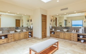A spacious bathroom with two sinks, wooden cabinetry, a bench, and a large mirror. - Diamante Golf Villa 22 (Cabo San Lucas)