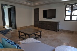 A living room with a dark wooden coffee table, a sofa with patterned cushions, a television on the wall, and a dark wooden cabinet. - Diamante Golf Villa 39 (Cabo San Lucas)