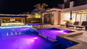 A swimming pool with a night-time lighting feature, surrounded by lounge chairs and a small patio area. - Diamante Golf Villa 39 (Cabo San Lucas)