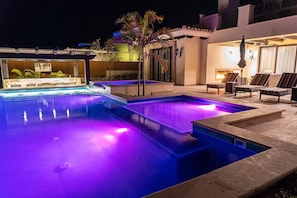 Ein Schwimmbecken mit nächtlicher Beleuchtung, umgeben von Liegestühlen und einer kleinen Terrasse.