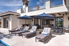A poolside area with lounge chairs and umbrellas, a barbecue grill, and a view of a residential building with a balcony. - Diamante Golf Villa 39 (Cabo San Lucas)
