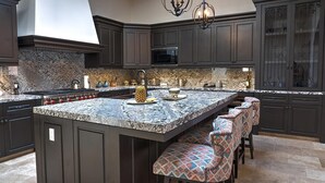 A modern kitchen with dark cabinetry, a granite countertop, and a central island with bar stools. - Diamante Golf Villa 39 (Cabo San Lucas)