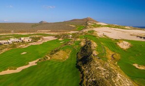 Un parcours de golf avec des bunkers, un club-house et une montagne en arrière-plan.