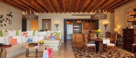 A spacious living area with a high wooden ceiling, a dining table set for four, and a kitchen in the background.