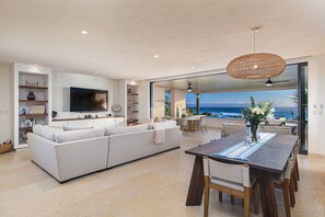 Ein modernes Wohnzimmer mit einer großen Couch, einem Esstisch und Blick auf den Ozean.