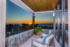 A balcony with a stone wall, a wooden ceiling, and a view of the sunset over the ocean. - 3 bed 3 5 bath  Private Pool Wide Ocean Views (Corral del Risco)