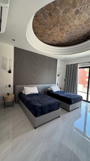 Quarto moderno com duas camas, parede de destaque em pedra e uma grande janela.