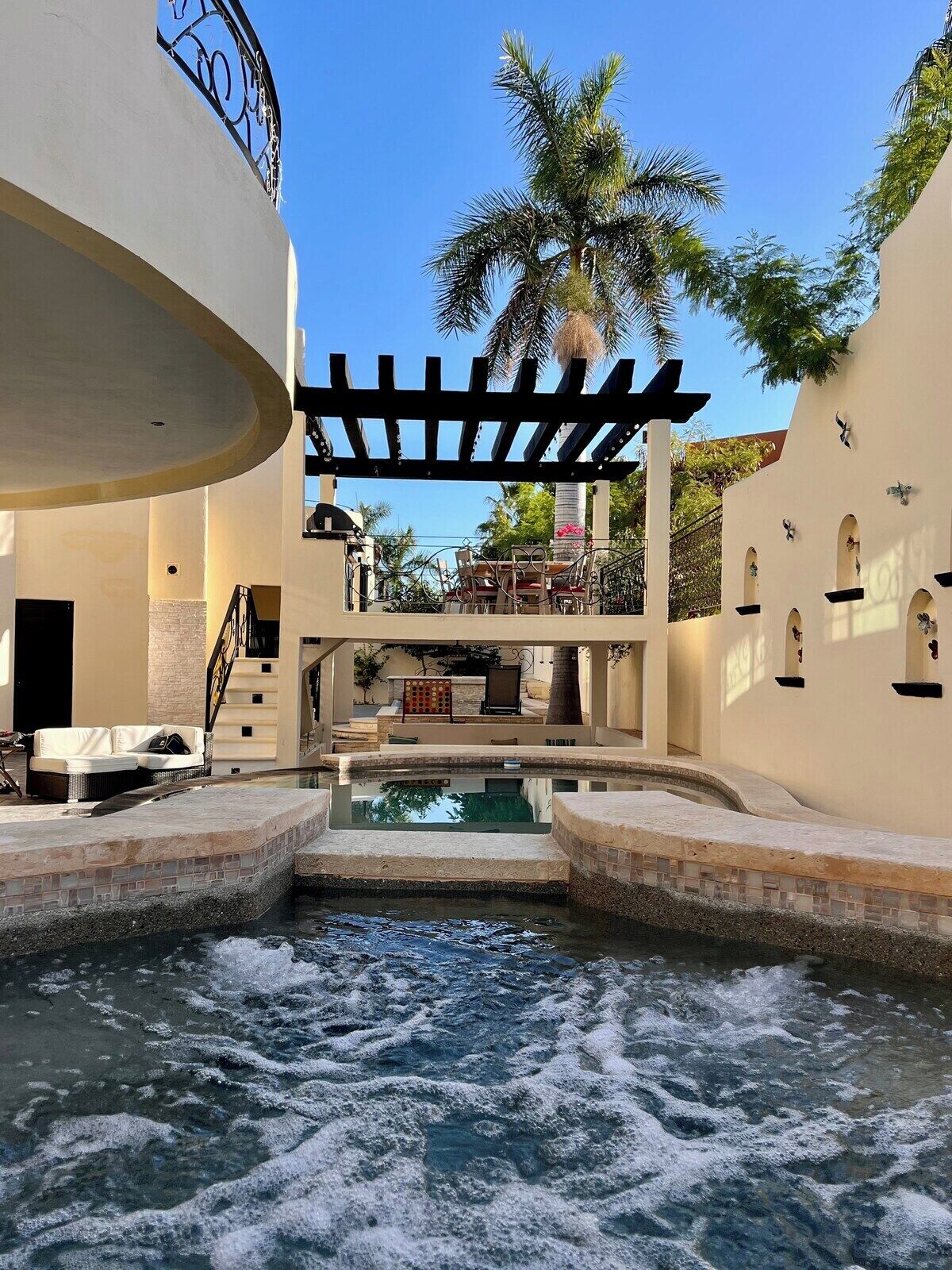 Zona de piscina amb cascada, seients i vista d'una palmera.