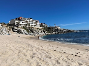 A beach with a hotel building, sandy shore, and rocky cliffs. - Grand Villa Famlee - multi-family rental sleeps 16 (Cabo San Lucas)