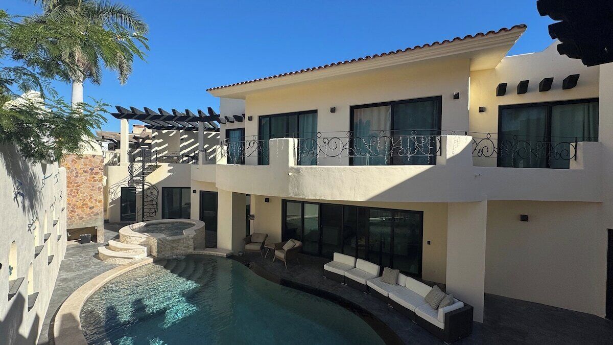 A two-story house with a swimming pool, outdoor seating, and a pergola.