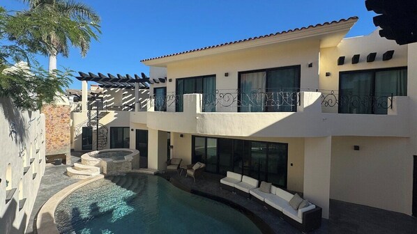 Uma casa de dois andares com piscina, área de estar ao ar livre e pérgula.
