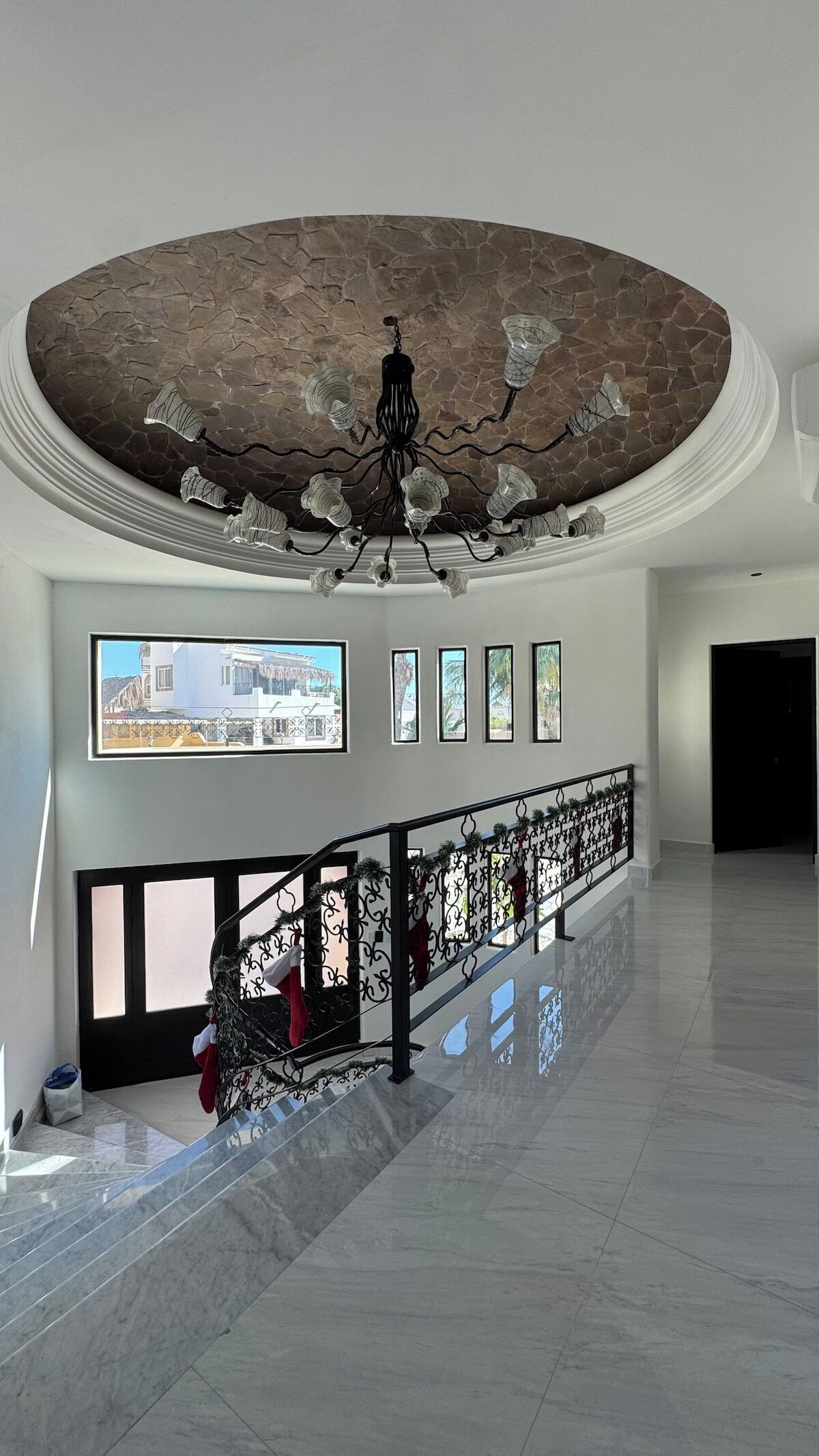 A spacious lobby with a high ceiling, a staircase with a railing, and a series of framed pictures on the wall.