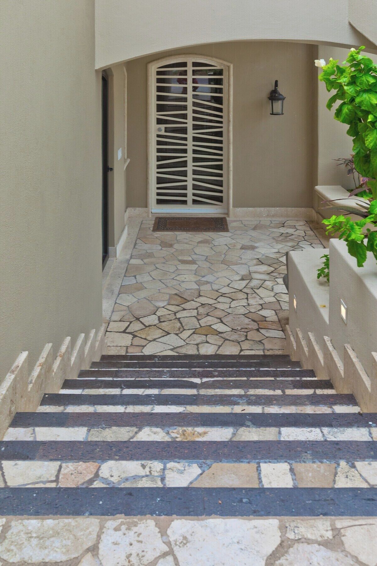 A stone staircase leading to a door with a decorative grille, a small lantern, and a potted plant.