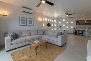 Ein modernes Wohnzimmer mit Ecksofa, Couchtisch und einer Küchenzeile mit Barhocker.
