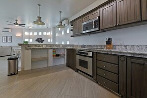 Une cuisine moderne avec des meubles en bois foncé, un plan de travail en granit, des appareils électroménagers en acier inoxydable et des luminaires suspendus.