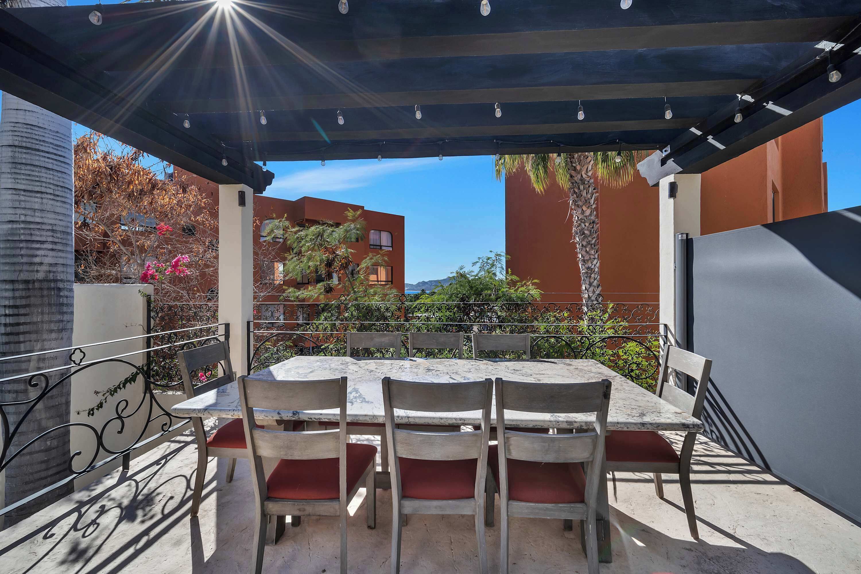 Eine Außenpatio mit Tisch und Stühlen, ein überdachter Pergola und im Hintergrund Gebäude und Bäume.