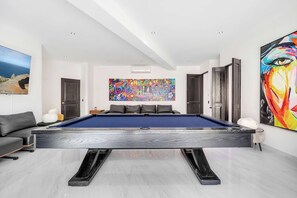 Ein modernes Wohnzimmer mit Billardtisch, einer Couch und einem großen, abstrakten Gemälde an der Wand.