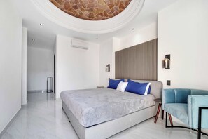 Ein modernes Schlafzimmer mit einem großen Bett, einem blauen Sessel und einer Steindecke.