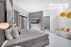 Ein modernes Schlafzimmer mit einem großen Bett, einer Couch, einem Fernseher und Blick ins Freie.
