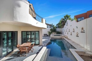 Una casa moderna amb piscina, zona de dinar amb taula i cadires, i un balcó amb barana.