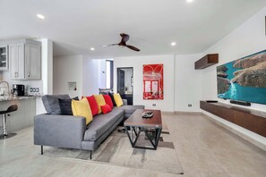 A modern living room with a grey sofa, a wooden coffee table, and a large flat-screen TV on a wooden stand. - Marbella Lane PrimeVilla n Modern Home Comfort (Cabo San Lucas)