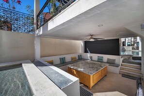 A modern outdoor living area with a marble table, wooden benches, and a ceiling fan. - Marbella Lane PrimeVilla n Modern Home Comfort (Cabo San Lucas)